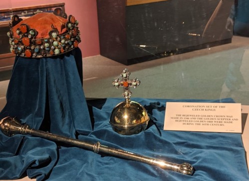 A crown, scepter, and orb displayed on blue fabric, labeled as the coronation set of the Greek kings from the 19th century.