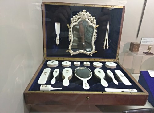 A vintage grooming set displayed in a wooden case, featuring a mirror, brushes, and various tools on a blue velvet background.