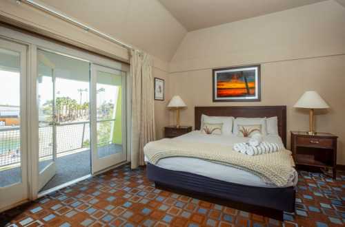 Cozy hotel room with a bed, nightstands, and a balcony overlooking palm trees and a scenic view.