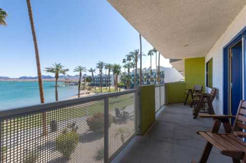 Balcony view overlooking a serene lake with palm trees and a clear blue sky.