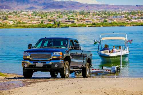 A black pickup truck parked by the water, with a boat being launched in the background against a scenic landscape.