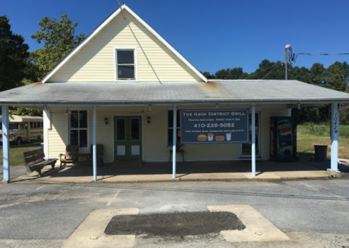 A yellow building with a sign for "The Neck District Grill" and a porch, set in a rural area.