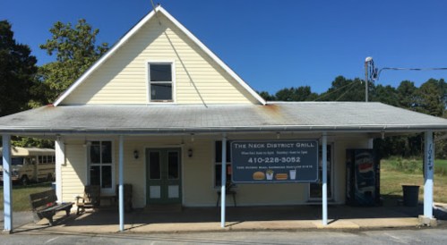 A yellow building with a sign for "The Neck District Grill" and a Pepsi advertisement outside on a clear day.