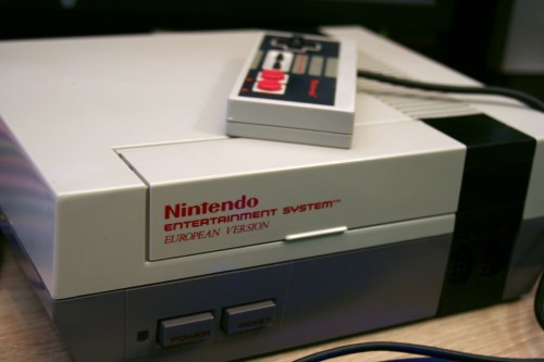A close-up of a Nintendo Entertainment System console with a controller on top, featuring the European version design.