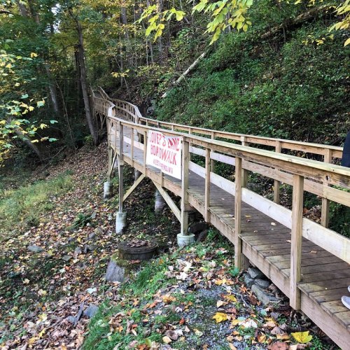 A wooden boardwalk leads through a forested area, with a sign indicating "Love's Way Boardwalk."