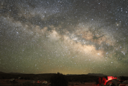 A stunning night sky filled with stars and the Milky Way, with silhouettes of trees and distant mountains below.