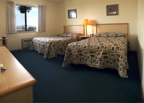 A cozy hotel room with two beds, wooden furniture, and a window showing a view outside.