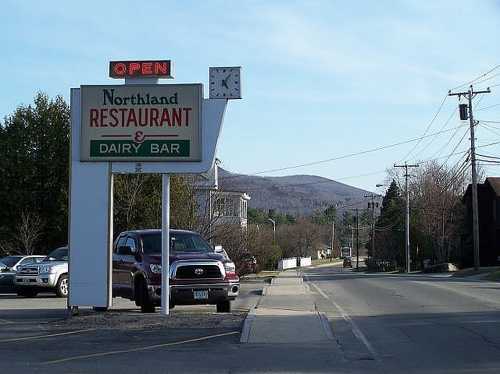 Sign for Northland Restaurant & Dairy Bar with a clock, set against a backdrop of mountains and a clear sky.