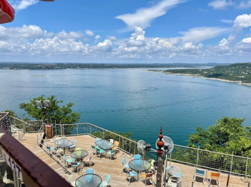 Scenic view of a lake from a deck, surrounded by trees and under a blue sky with fluffy clouds.