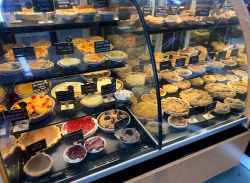 A display case filled with various pies and desserts, labeled with names and prices.