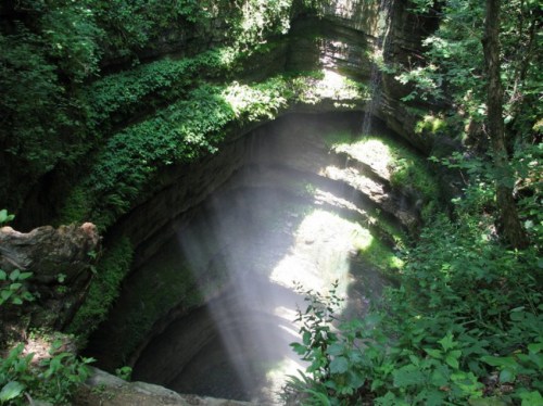 A deep, lush green canyon with sunlight streaming down into the water below, surrounded by dense foliage.