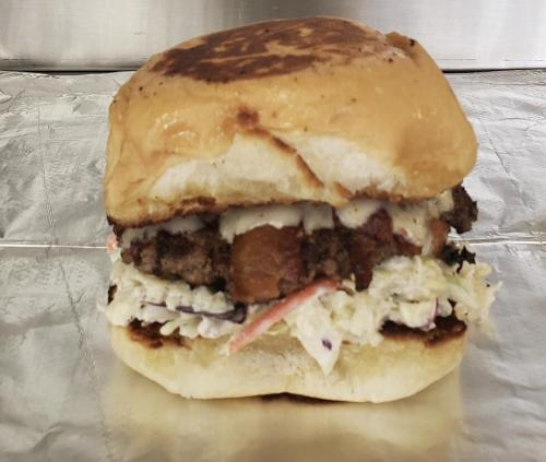 A close-up of a burger with a toasted bun, beef patty, coleslaw, and a slice of melted cheese.