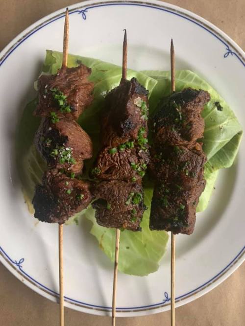 Three grilled meat skewers garnished with green herbs, resting on a bed of lettuce on a white plate.