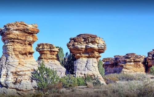 Rock formations with unique shapes and textures against a clear blue sky, surrounded by sparse vegetation.