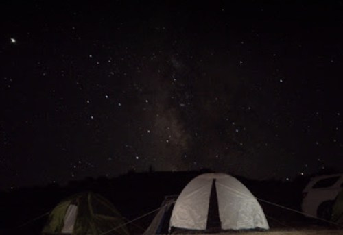 Tents set up under a starry night sky, with the Milky Way visible in the background.