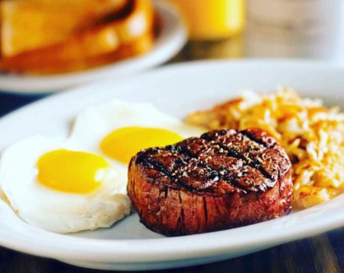 A plate with two sunny-side-up eggs, a grilled steak, and crispy hash browns.