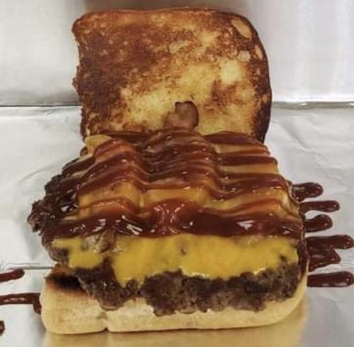 A cheeseburger with bacon and barbecue sauce on toasted bread, served on aluminum foil.