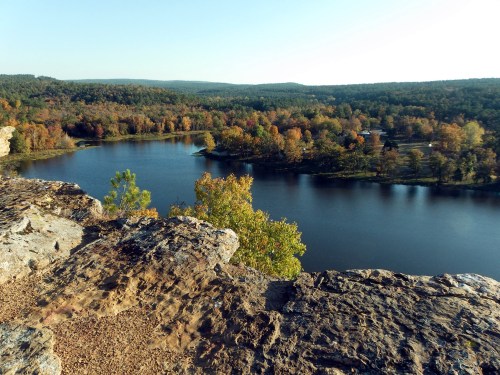 A scenic view of a river surrounded by colorful autumn trees and rolling hills under a clear blue sky.