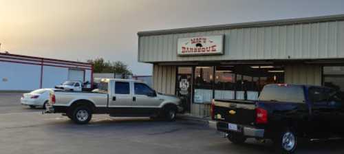 Exterior of Matt's Barbecue, featuring a metal building with large windows and parked trucks in the foreground.