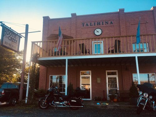 A red brick building with a clock, featuring a sign for "Hootie Creek" and parked motorcycles in front.