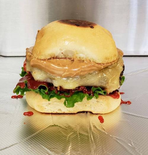 A burger with a toasted bun, lettuce, ketchup, and a layer of peanut butter on top of a patty.