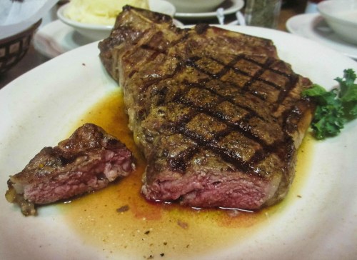 A perfectly cooked steak with a grilled surface, served on a plate with a small piece cut off, showcasing its juicy interior.
