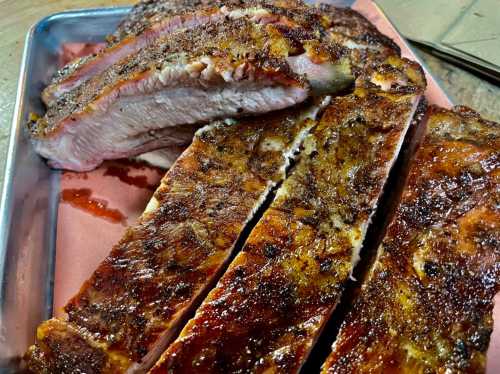 Close-up of sliced, smoked brisket on a metal tray, showcasing a crispy, seasoned crust and juicy interior.