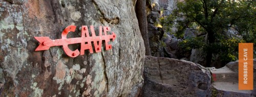 A red sign reading "CAVE" on a rocky surface in a natural outdoor setting, with trees in the background.