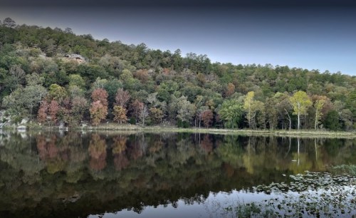 A serene lake reflecting colorful trees and a hillside, showcasing autumn foliage and calm waters.