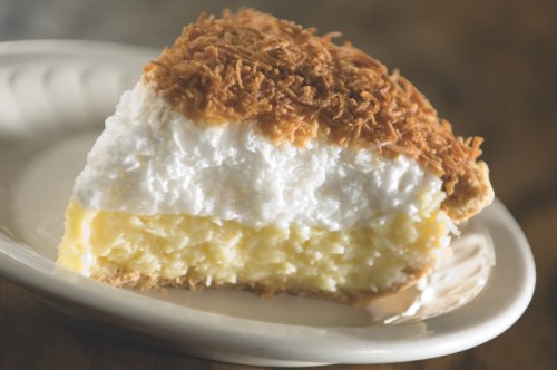 A slice of coconut cream pie with a golden toasted topping on a white plate.