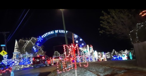 Colorful holiday lights illuminate a festive scene, featuring a sign that reads "Festival of Lights" at night.