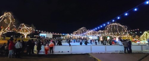 A lively outdoor ice skating rink at night, surrounded by trees adorned with colorful lights and festive decorations.