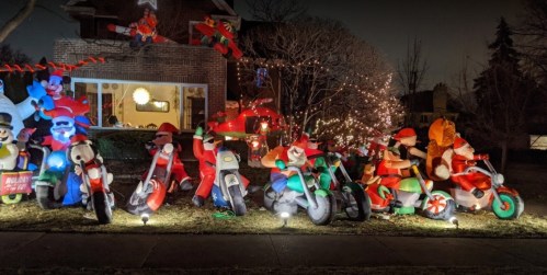 Colorful holiday decorations featuring inflatable Santa figures on motorcycles, with lights and festive elements in a yard.