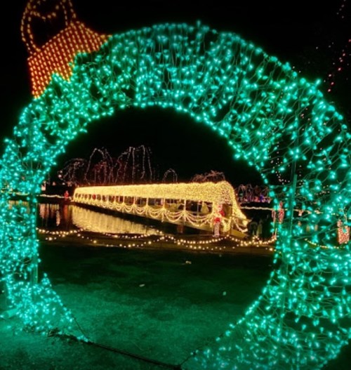 A glowing green archway frames a bridge adorned with colorful lights, reflecting on the water at night.