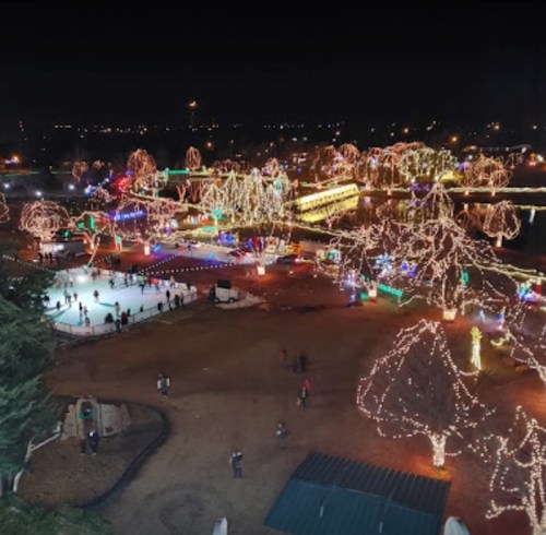Aerial view of a park illuminated with colorful holiday lights, featuring ice skaters and decorated trees at night.