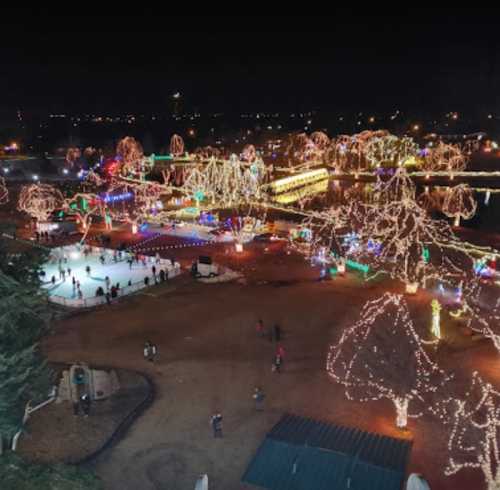 Aerial view of a park illuminated with colorful holiday lights, featuring ice skaters and decorated trees at night.