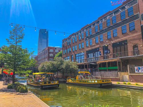 Two yellow boats on a canal, surrounded by greenery and historic buildings under a clear blue sky.