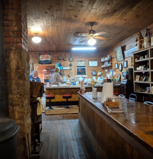 A cozy, rustic interior of a café with wooden walls, a bar counter, and staff preparing food in the background.