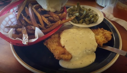 A plate featuring fried chicken with white gravy, green beans, and a side of crispy fries in a basket.