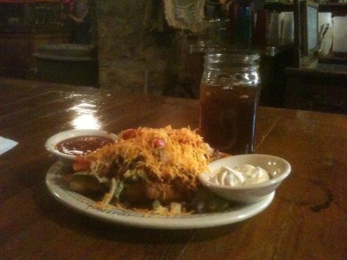 A plate of loaded nachos topped with cheese, tomatoes, and lettuce, served with salsa and sour cream, alongside iced tea.
