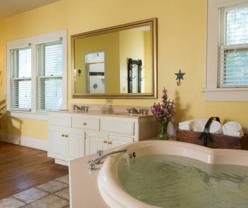 Bright bathroom with yellow walls, a large mirror, a soaking tub, and a vanity with flowers and neatly arranged towels.