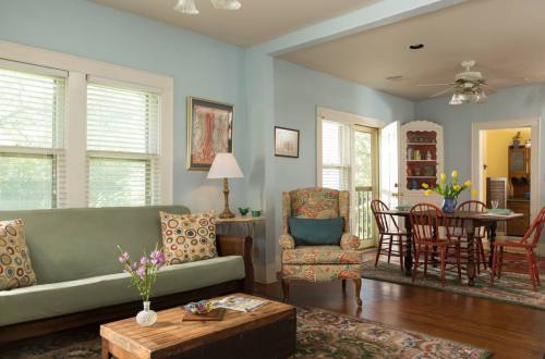 Cozy living room with a green sofa, patterned chairs, a wooden coffee table, and a dining area in a bright, airy space.
