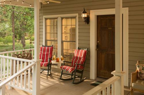 A cozy porch with two rocking chairs, a small table, and warm lighting, surrounded by greenery.