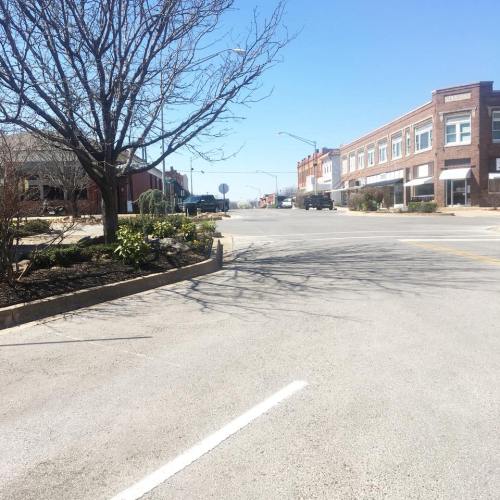 A quiet street scene with a clear blue sky, lined with brick buildings and a bare tree on the left.