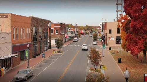 A quiet downtown street lined with shops and trees, showcasing autumn colors and a clear blue sky.
