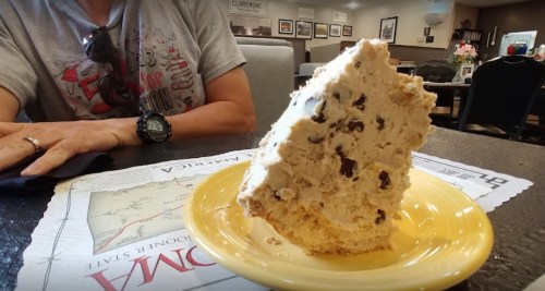 A large slice of chocolate chip ice cream cake on a yellow plate, with a person’s arm and watch in the background.