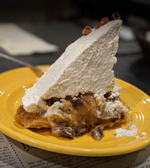 A slice of pie with a thick layer of whipped cream on top, resting on a yellow plate.