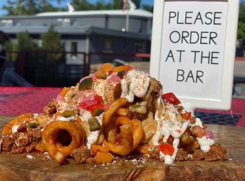 A plate of loaded curly fries topped with colorful toppings and a sign that says "Please order at the bar."