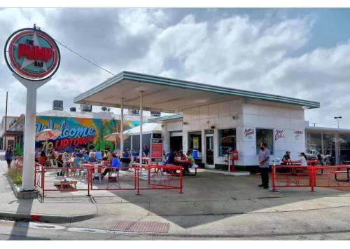 A vibrant diner with outdoor seating, colorful murals, and a retro sign, bustling with customers enjoying their meals.