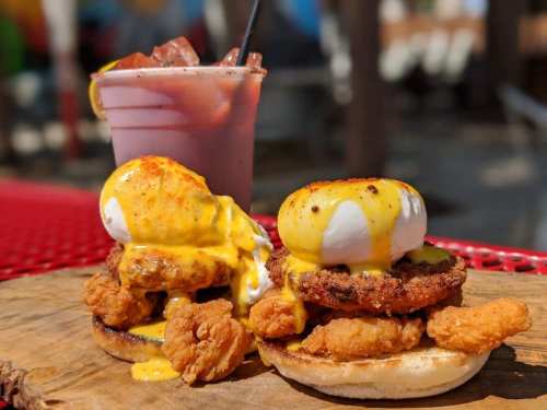 A plate featuring a stacked chicken and egg dish with hollandaise sauce, alongside a colorful drink.